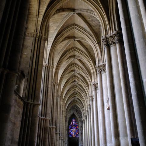 The vaulted ceilings of a gothic cathedral with a stained glass window in the distance, embodying the architectural splendor of the past.