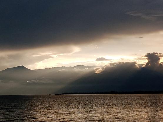 Sunsubiro sur la Tanganjika lago. La nuboj kunfondigas kun la montetoj en la horizonto.