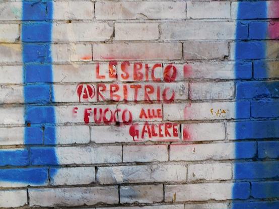 another stencil art  on a wall ,  now in red,  reading  "LESBICO  ARBITRIO  E FUOCO  ALLE GALERE"  (translation in caption) ;    there's a circle surrounding the first letter 'A',  resembling the anarchist symbol