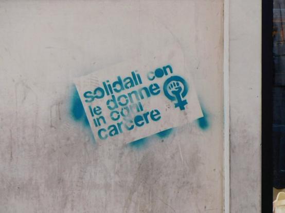 another stencil text,  now in blue;   "solidali con le donne in ogni carcere"  (translated in caption)  and also the left fist  united with the Venus symbol  on the right