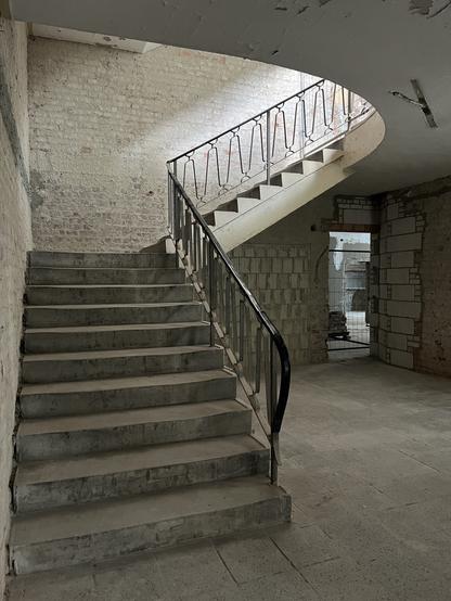 Betontreppe mit schwarzem Metallgeländer in einem Gebäude mit freiliegenden Ziegelwänden und unvollendeter Konstruktion.