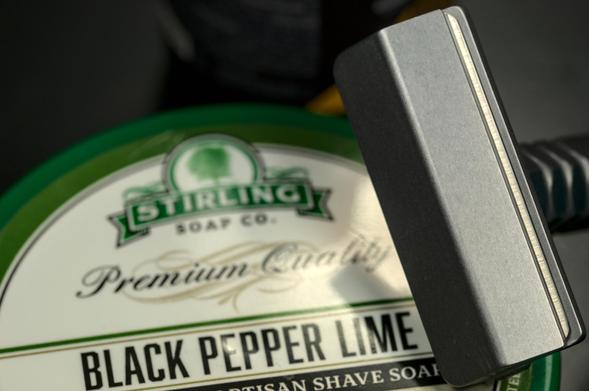 A closeup of the head of an Alumigoose razor leaning on a tub of Stirling Black Pepper Lime soap