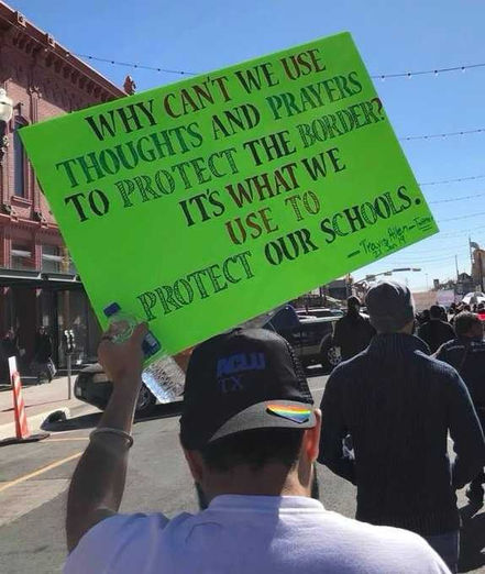 photo of protestors with one holding a hand lettered sign "Why can't we use thoughts and prayers to protect the border? It's what we use to protect our schools."