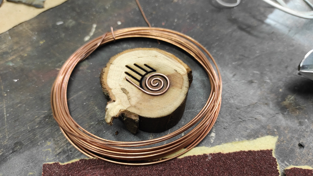 The same artwork as in the previous description, with the spiral section of the laser-engraved symbol now filled with copper wire during the inlay process.