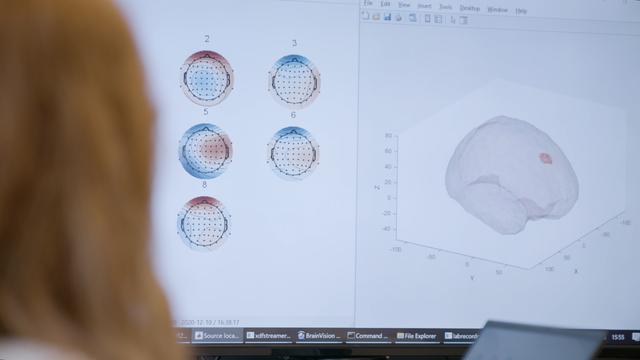 Das Bild zeigt einen Computerbildschirm, auf dem Daten eines neurologischen Experiments bei Zander Labs zu sehen sind. Links auf dem Bildschirm sind mehrere grafische Darstellungen von Kopfformen mit markierten Zonen und Punkten, wahrscheinlich Elektrodenpositionen eines EEG. Rechts ist eine dreidimensionale Darstellung eines Gehirns mit einer hervorgehobenen Region zu sehen, hier werden die Gehirnaktivität analysiert. Im Vordergrund erforscht eine Wissenschaftlerin die elektrischen Quellen im Gehirn, aus denen bestimmte Aktivitäten entstehen.
Foto: Copyright „Gedachtegoed“