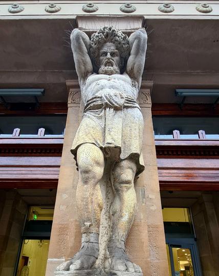 A large male sculpted figure acting as a pillar on the facade of a Victorian building.