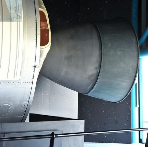 An indoor photograph of a black bell-shaped nozzle emerging from the back of a metallic cylinder. The nozzle has a dull black color.