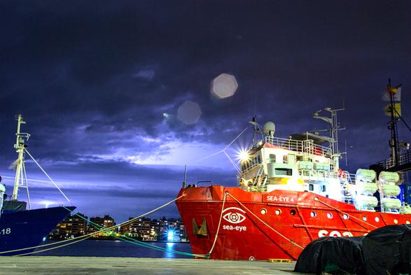 Bild bei NAcht, im Vordergrund das rettungsschiff sea-eye4 am pier, im hintergrund die stadt burriana, der himmel ist dunkel bewölkt abre durch blitze hell erleuchtet