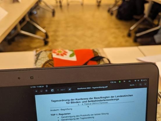 Foto aus dem Konferenzraum. Unscharf sind im Hintergrund die Tischbeine zu sehen. Im Vordergrund ein Teil eines Laptopbildschirmes mit dem Text:
Tagesordnung der Konferenz der Beauftragten der Landeskirchen für Blinden- und Sehbehindertenseelsorge
5. – 6. Februar 2024 in Hannover
Andacht / Begrüßung
TOP 1: Regularien
Genehmigung des Protokolls der letzten Sitzung
Genehmigung der Tagesordnung