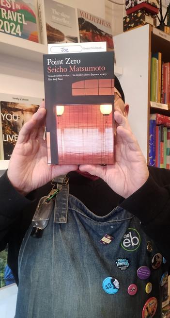 Bookseller Joe holding up a copy of Point Zero by Seicho Matsumoto, to recommend it in the Edinburgh Bookshop
