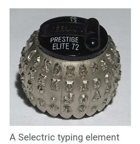 Photo of a piece of old technology: the "font ball" from a 1970s/1980s electric typewriter. The spherical object has a black plastic top (like a lid, but not quite), and an open hollow bottom. Around the sides is a myriad of letters and symbols in a specific font. In this photo, the top indicates that the font is "Prestige Elite 72." 

The caption for the image reads, "A Selectric typing element."