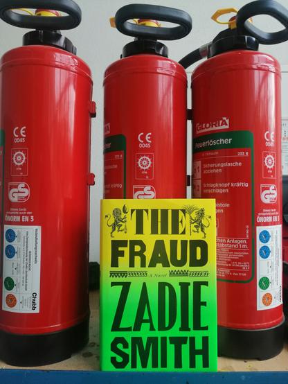 Zadie Smith's novel The Fraud is pictured in front of 3 fire-extinguishers