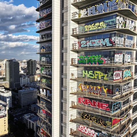 Photo showing about ten floors in the middle of an abandoned glass condo tower in downtown Los Angeles with cloudy blue sky in the background. Every floor is absolutely covered with beautiful, colorful, incredibly high quality LA style graffiti tags.