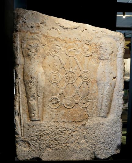 🪔 Above phalerae are two partially chipped off bracelets (armillae), followed by the remains of two necklaces (torques), and a larger central wreath (corona). 
🪔 The image is framed by two greaves (Lat. ocreae), while a centurion's rod (uitis) can be seen between the left greave and the edge of the monument. 
🪔 The central phalera features the motif of the head of Medusa (gorgoneion), while another three figurative phalerae depict two portrait busts and the Roman she-wolf.