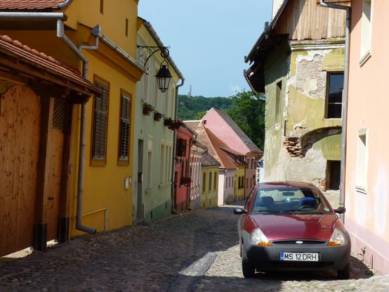 colourful old houses, of vernacular architecture, line the shadowed street. only a modern car dates the photograph as a recent one.