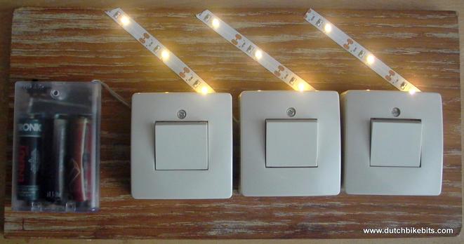 A piece of wood with light switches, LEDs and a battery pack.