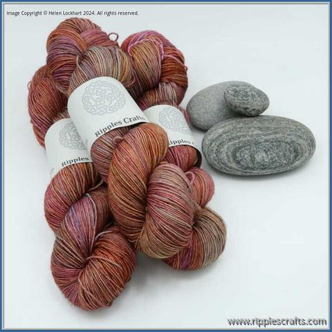 3 hanks of yarn in a small pile with some grey rocks alongside them. The yarn is a mix of oranges, pinks and blues.