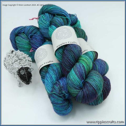 3 hanks of yarn with a beaded sheep alongside them. The yarn is a mix of greens and blues