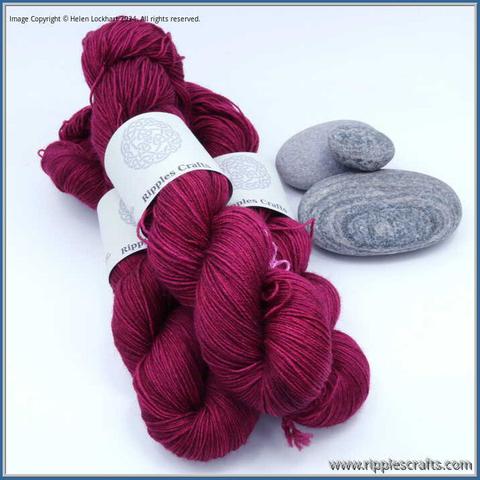 3 hanks of yarn with 3 grey rocks alongside them.  The yarn is a deep plum shade.