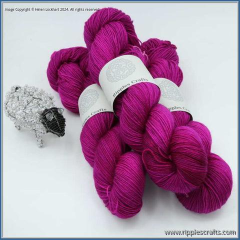 3 hanks of yarn with a beaded sheep alongside. The yarn is an intense berry pink shade