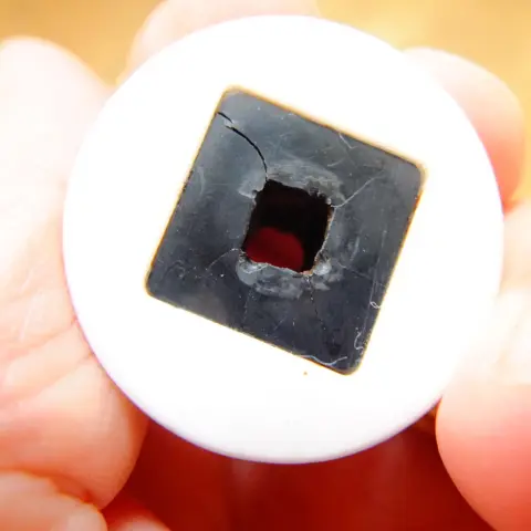 The bottom face of the ceramic grinder part that attaches to the square shaft that is turned to grind the coffee - the square section of black plastic embedded into the ceramic grinder part is now cracked with several cracks radiating from the square hole in the centre