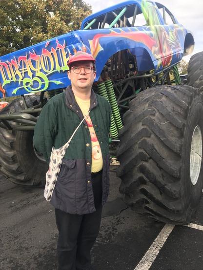 Eine männliche Person steht vor einem blau-bunten Monstertruck.