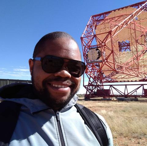 Dr. Gopolang Mohlabeng, a smiling Black man wearing sunglasses, stands outdoors beside a large sensor.