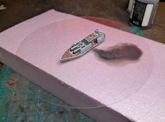 1/1200 wargaming ship painted on a plastic disk to look like it's leaking oil