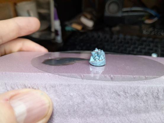 1/1200 wargaming ship painted on a plastic disk to look like it's leaking oil, from the rear to show the tilt of the boat better