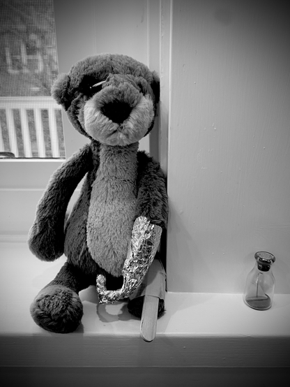 Otter stuffed toy dressed as a pirate with eyepatch, tinfoil hook and popsicle stick peg leg sitting upon window sill.