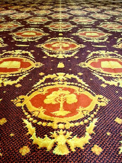 A burgandy and black checked carpet with a repeating red and gold design featuring the Glasgow coat of arms.