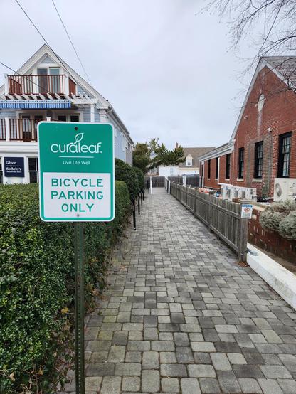 A business sign for Bicycle Parking Only, in front of a wide, paver area leading to many bicycle parking racks beside the business.