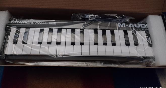 M-Audio Mini Midi M32 Keyboard in a half open box, wrapped in plastic and secured with packing foam end caps.