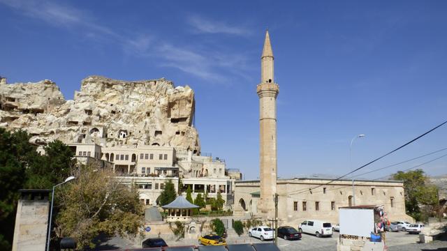 Against a blue sky, pale cliffs with cave houses, and the minaret of the old mosque