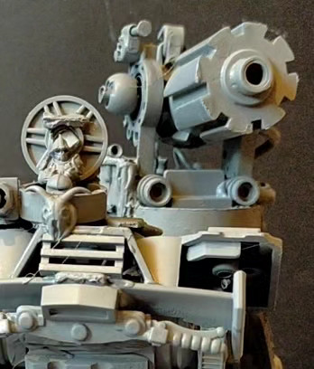 The image shows a close up detail of a scale model tank from a 3/4 front view, from a low angle. Here you can see the tank commander model in his hatch, the from of which is decorated with an animal skull from an old 28mm fantasy character sprue.

From the same roughly 15/20mm Tonk build. All made out of stuff from my junk plastic and craft stuff trays.