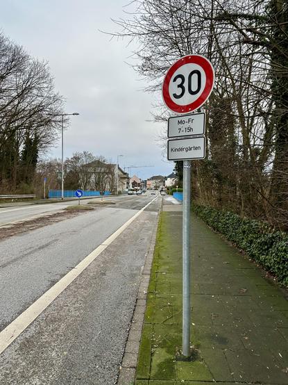 Zu sehen ist das Schild für Tempo 30, Mo-Fr 7-15h, Kindergarten an der Saarner Straße. Auch sind die blauen Geländer der Brücke über die Rheinische Bahn zu sehen. Auf der Rheinischen Bahn soll der Radschnellweg 1, RS1, entstehen.