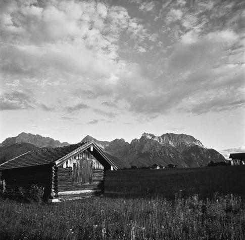 Monochrome image of a tiny hay house in front of mountains.