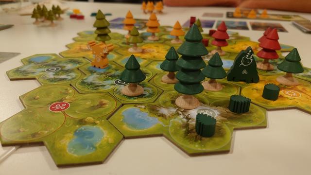 Spielaufbau von "Forests of Pangia" - auf Hexfeldern mit verschiedenen Landschaftsarten stehen kleine Bäume aus Holz in verschiedenen Größen und Holzmeeples von mystischen "Waldgeistern"