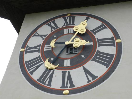 The clock tower in Graz. Detail of one of the clocks. Black dials with golden arrows. The clock is in black with red accents.