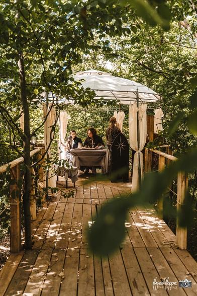 A wooden platform above ground, framed by tree branches. It has a pavillon with some elves sitting underneath.