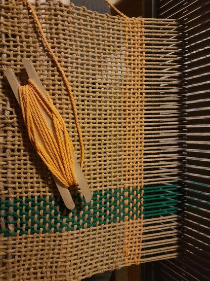 Un début de tissage très souple en gros coton pour macramé. La chaîne est majoritairement nature,  avec une petite bande vert forêt légèrement à droite. La trame vient de changer du nature vers le jaune doré,  amorçant un motif à carreaux.