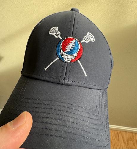 A hat with lacrosse sticks intersecting behind a Steal Your Face