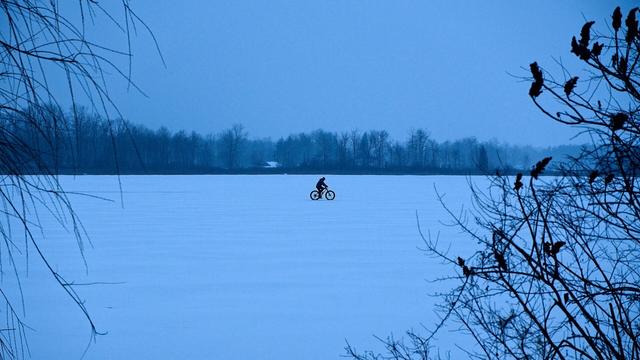 Silhouette of a man riding his bike across a frozen lake.