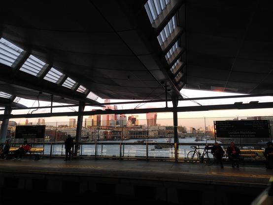 A photo taken across a trainline, showing the opposite platform, and beyond it the River Thames with a city skyline further beyond
