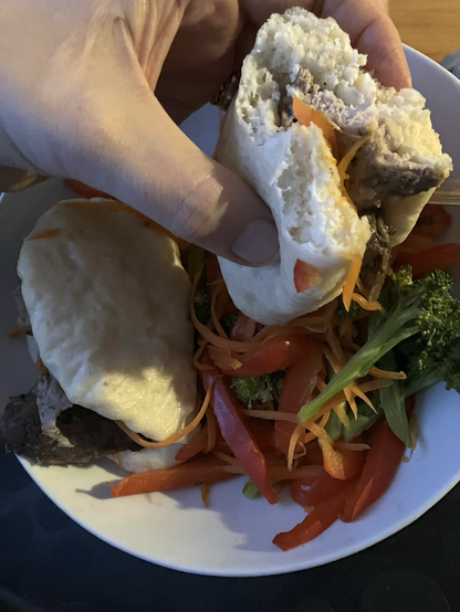 The airy inside of the bao visible with the dish filled with vegetables and a second bao.