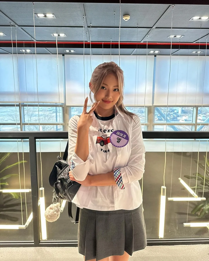 Kpop idol Yel faces the camera and makes a V-sign with her palm turned inward towards herself.