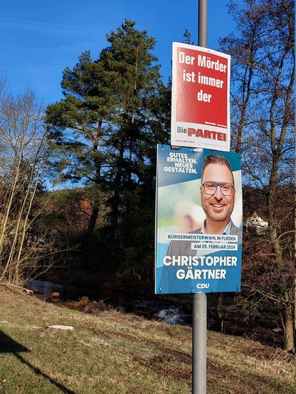 Wahlplakat der Partei 'Die PARTEI' mit der Aufschrift "Der Mörder ist immer der" über einem Plakat des CDU Bürgermeisterkandidats Christopher Gärtner mit der Aufschrift "Gutes erhalten. Neues gestalten."