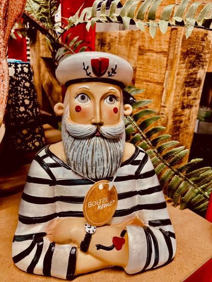 Pottery sailor with arms folded stripe blouse grey beard and red spots on his cheeks. His rolled up arm sleeve has a heart tattoo. Handsome guy.