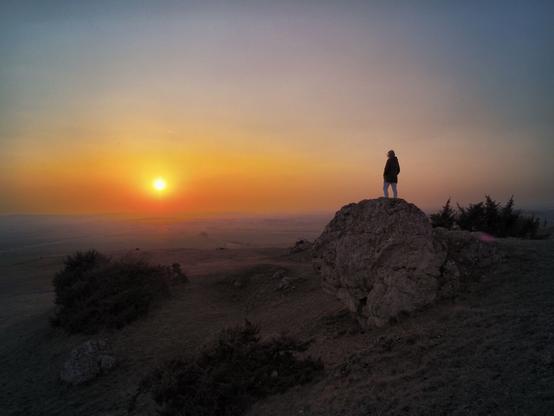 The Nördlinger Ries is not only a peculiar landscape formed by a huge meteor impact, but also an agricultural area full of beauty and wonderful photo spots. This photo was taken on the Rollenberg at sunset. You can see the circular plain of the crater in the warm sunlight. On the right there is a person standing on a huge rock, looking across the plain into the setting sun. A scene full of the warmth of the sun, even though it was shot in winter. 😊