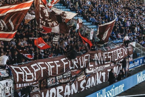 Blick in die Kurve des fcsp in Magdeburg vorne Transparente:ABFIFF FÜR DFL INVESTOREN
darunter: VORAN SANKT PAULI 
Hinter dem Zaun Menschen mit der Pauli Fahnen.
